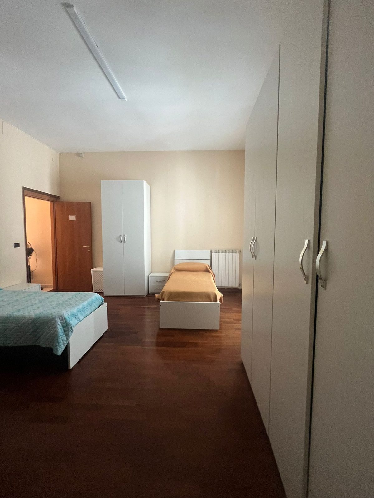 Camera con letto matrimoniale e letto singolo su pavimento in parquet nella comunità Happy Family