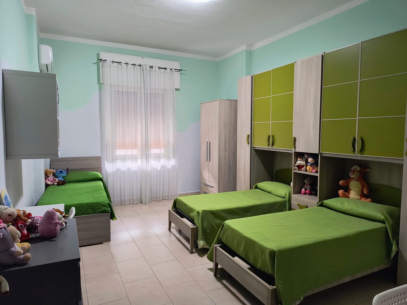 Cameretta con letti singoli verdi e peluche nella comunità Piccoli Eroi