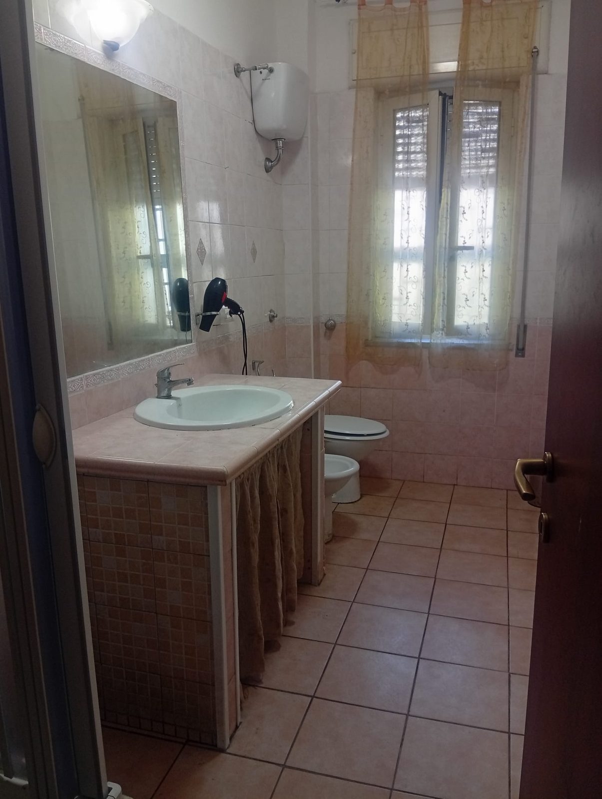 Bagno con lavabo, doccia e finestra con tende nella comunità State Buoni se Potete